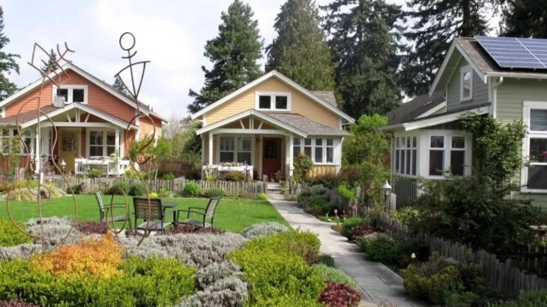 Three cottages surrounding a lawn and nicely landscaped pathway. 